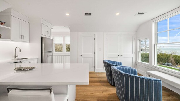 Una cocina moderna con armarios blancos, una isla central y vistas al exterior a través de amplios ventanales.