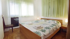 Un dormitorio con cama, una silla, una mesita de noche y una ventana con cortinas.