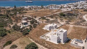 A coastal town with white buildings, a large ship in the sea, and a hilly landscape in the background. - Harites Home – Sea View Villa A | Peaceful Island Escape with Stunning Views (Milos)