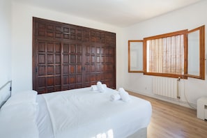 Un dormitorio con una puerta de madera grande, una cama con ropa de cama blanca y un ventanal con persianas de madera.
