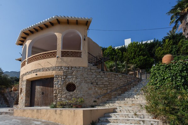 A stone building with a curved roof, a wooden door, and a staircase leading up to a balcony. - Holiday Home 'Villa Margarita' with Sea Views, Wi-Fi & Air Conditioning (Denia)