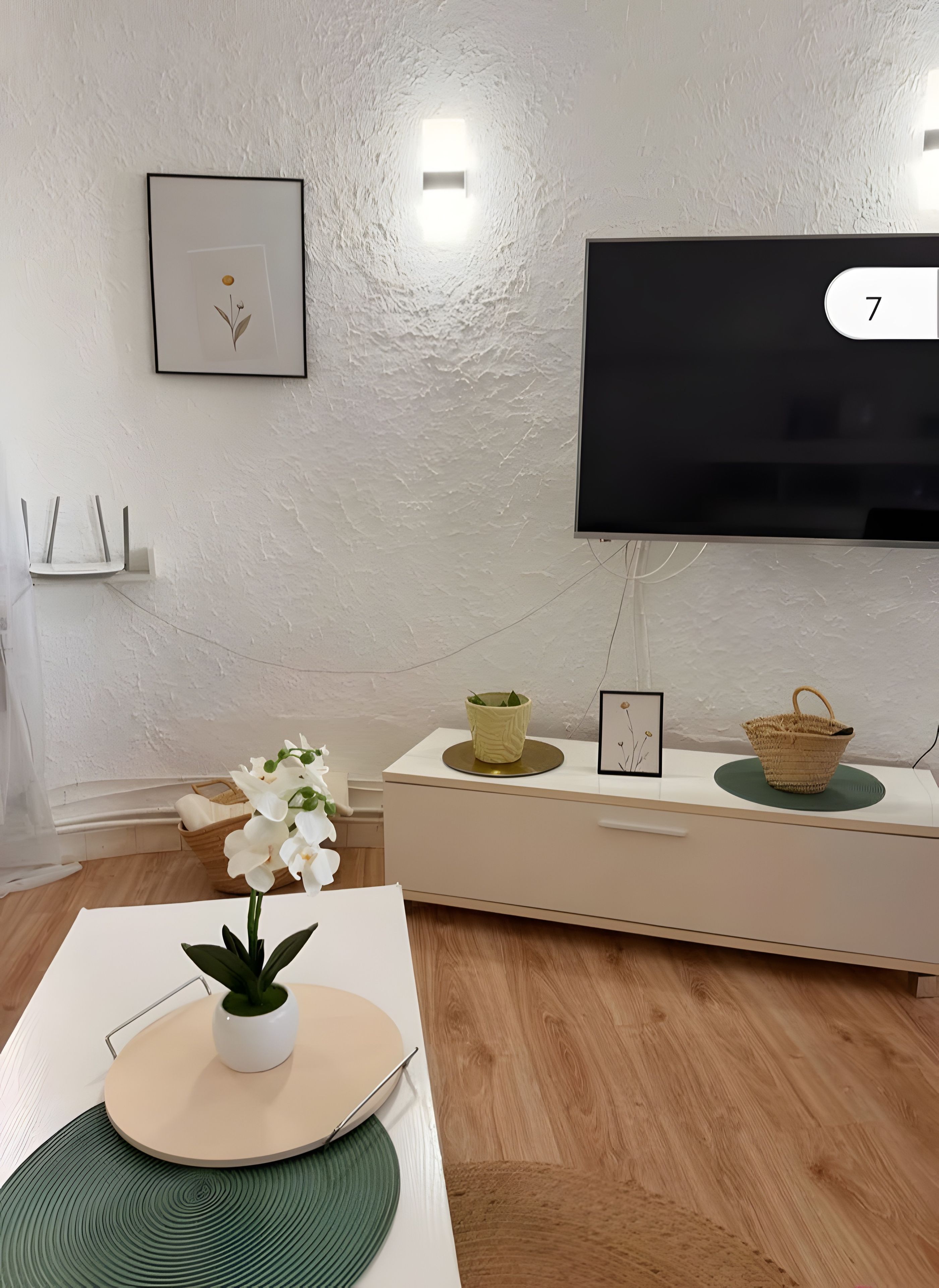 A modern living room with a flat-screen TV mounted on the wall, a white console table with decorative items, and a wooden floor.