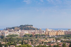 Un paisaje urbano costero con una fortaleza en la cima de una colina, edificios urbanos densos y una mezcla de construcciones residenciales y comerciales.