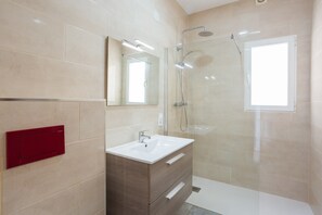 Un bagno moderno con cabina doccia in vetro, lavandino bianco e mobile vanitario in legno.