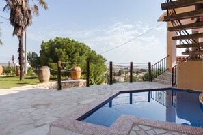 Una piscina con baldosas de piedra, una escalera de madera y vistas a un paisaje urbano.