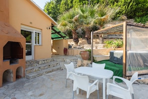 A patio with a stone floor, white plastic chairs, a table, a brick oven, and a greenhouse. - Holiday Home 'Villa Margarita' with Sea View, Wi-Fi and Air Conditioning (Denia)