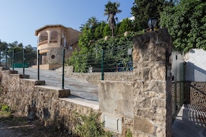 A stone wall with a metal gate, a stone staircase, and a building with arches in the background.