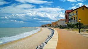 Ein Küstenweg mit Kieselsteinen, einem Sandstrand und Gebäuden mit Balkonen.