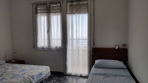 Quarto com duas camas, janela com cortinas leves, mesa de cabeceira e criado-mudo.