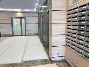 Un espace moderne pour les ascenseurs, avec un sol en marbre, un panneau mural en bois et un mur de boîtes aux lettres.