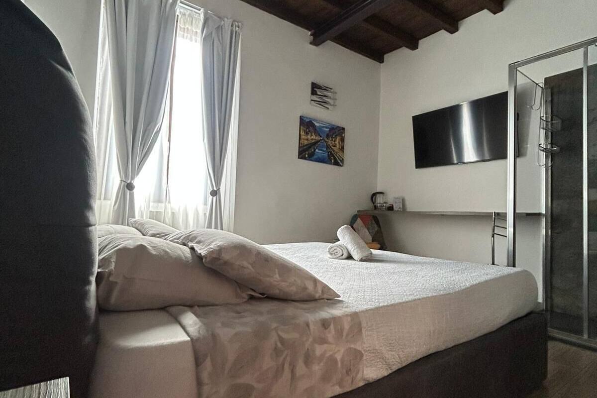 Une chambre à coucher avec un lit, un téléviseur fixé au mur et une fenêtre avec des rideaux.