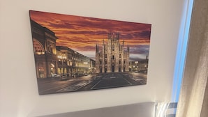 A hotel room with a large bed, a nightstand with a phone, and a painting of a cathedral on the wall.