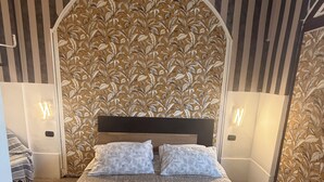 A neatly made bed with a floral-patterned headboard, two pillows, and rolled towels on the bed.