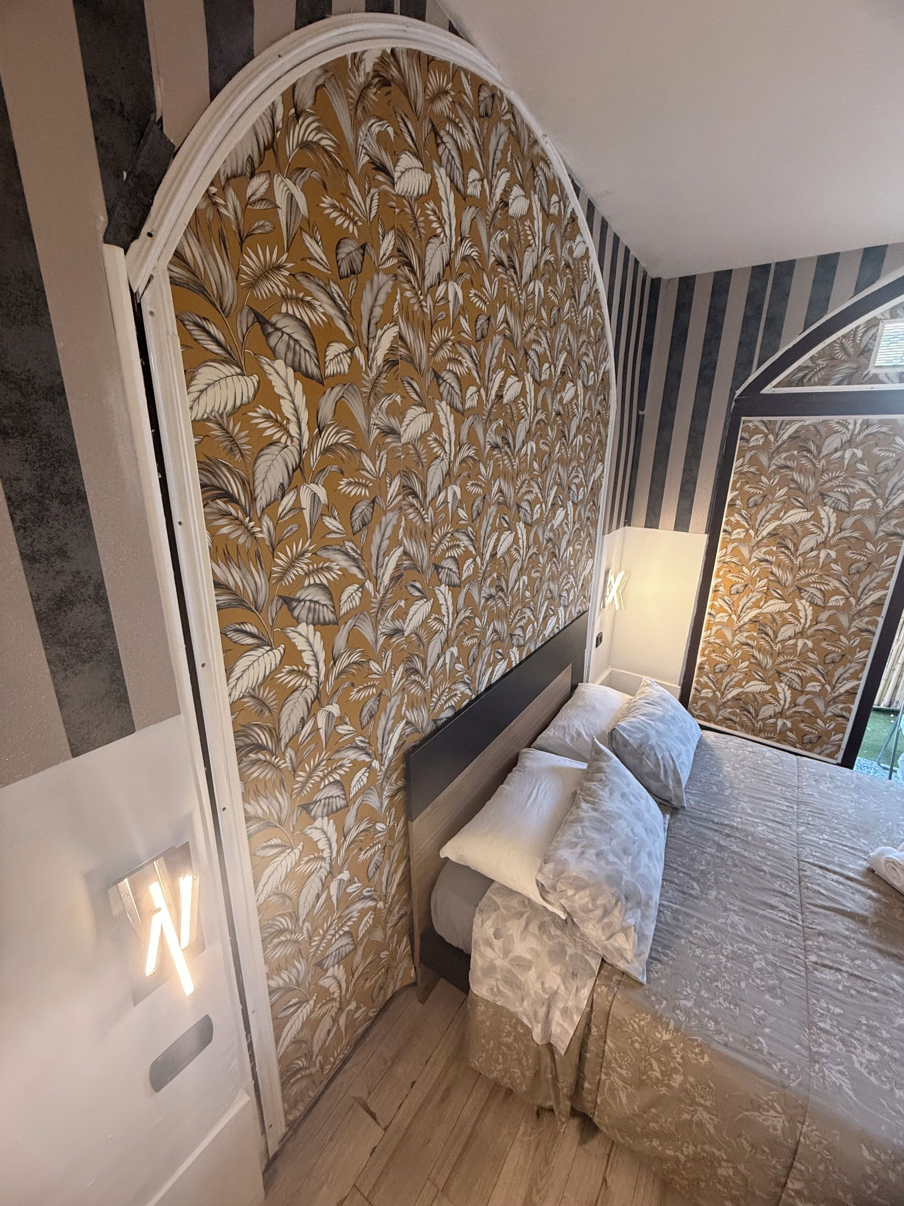A bedroom with a curved headboard, a bed with white linens, a nightstand, and a wall-mounted lamp.