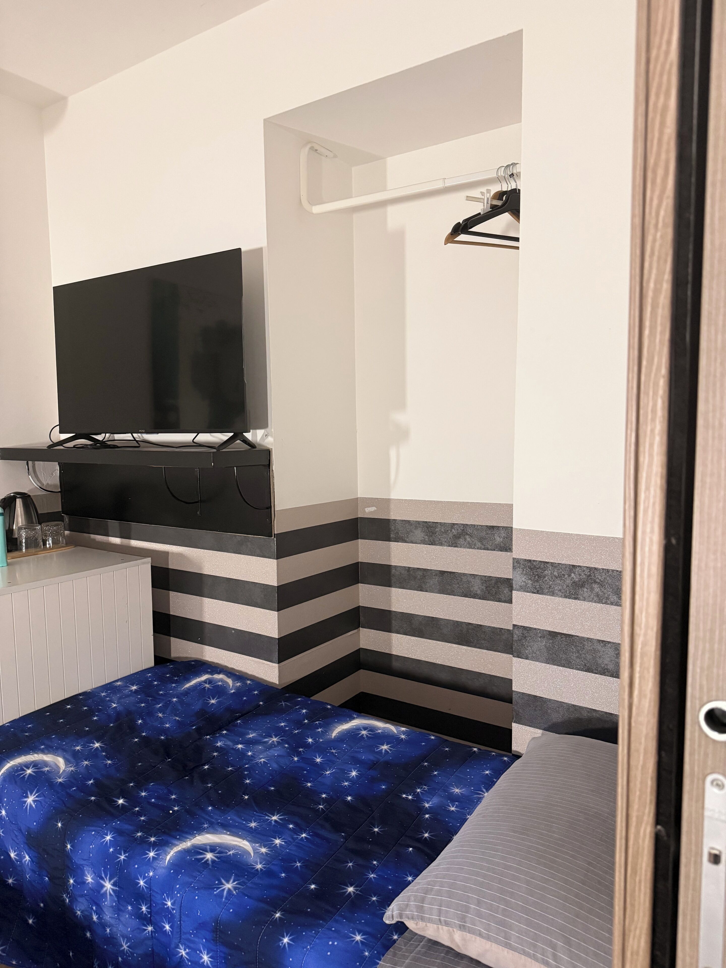 Ein Schlafzimmer mit Bett, Fernseher, einer kleinen Küchenzeile und einer Duschkabine.