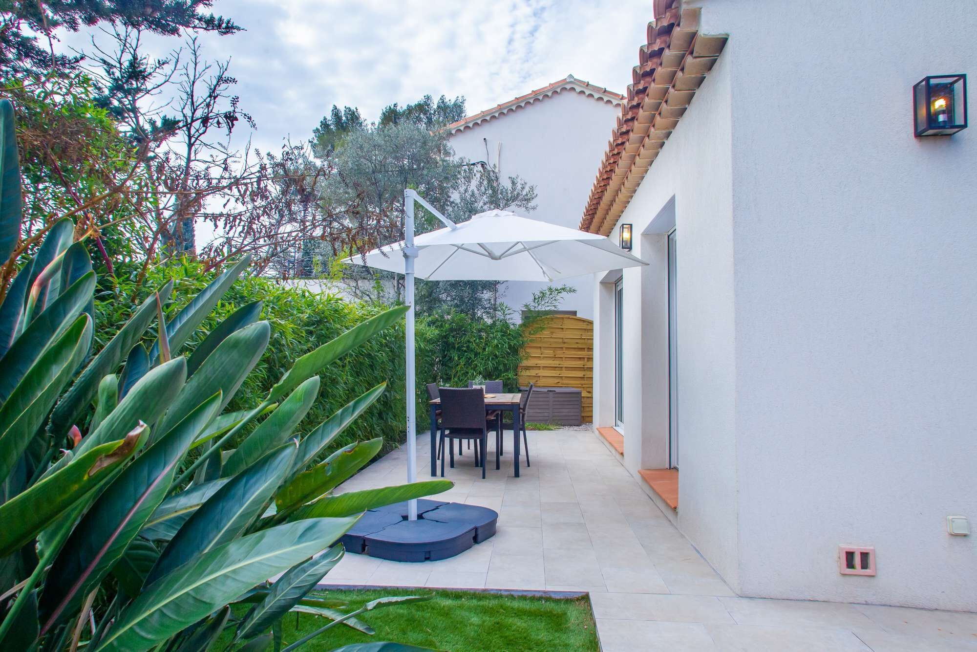 Un patio con una mesa, sillas, un paraguas blanco y una valla de madera.