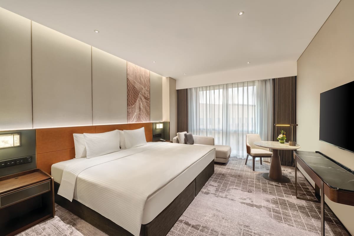 Habitación de hotel con una cama grande, un escritorio, una silla, un televisor y una ventana con cortinas.