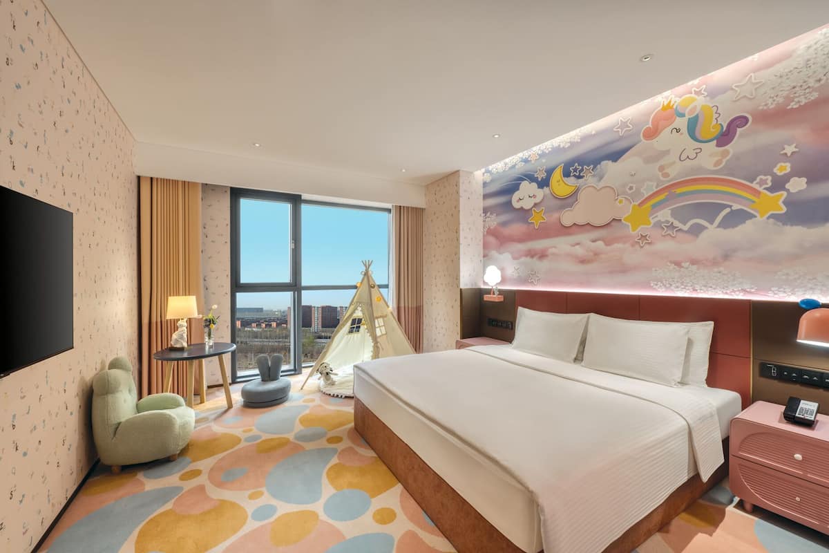 Una habitación de hotel con una cama grande, vistas de la ciudad, una tienda de campaña y un mural de nubes y estrellas.