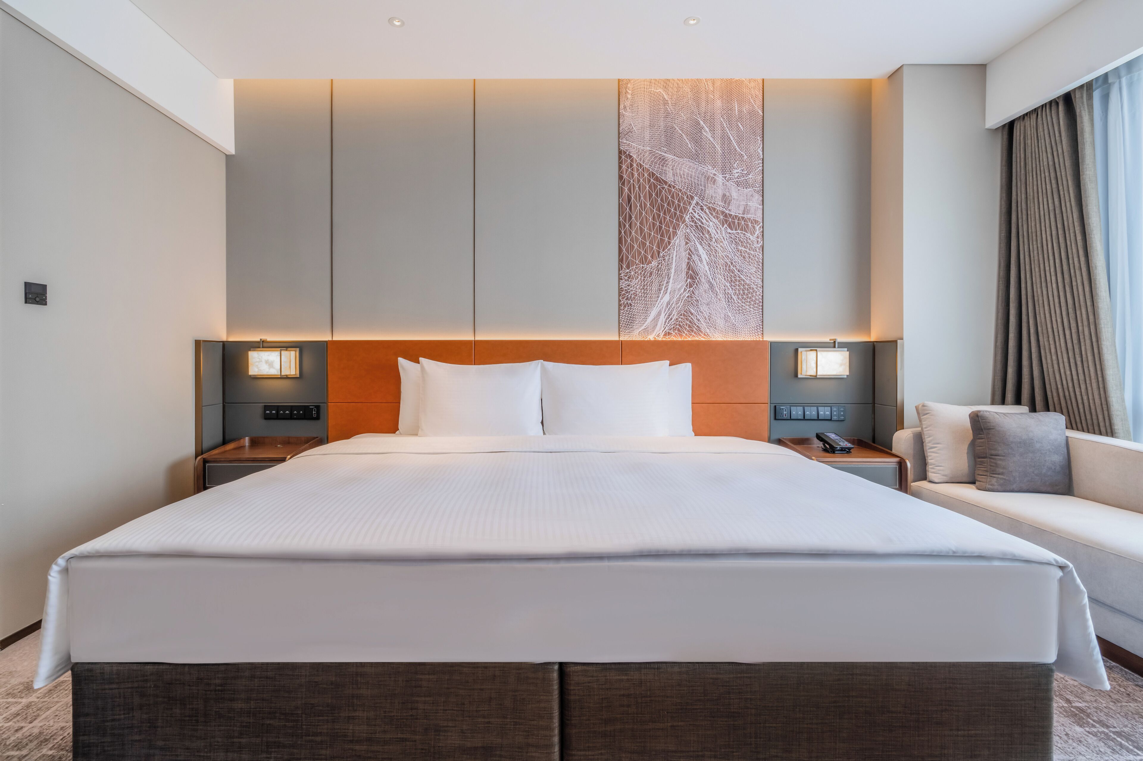 Una habitación de hotel con una cama grande, mesitas de noche con lámparas, un sofá y una obra de arte colgada en la pared.