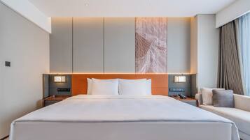 Una habitación de hotel con una cama grande, mesitas de noche con lámparas, un sofá y una obra de arte colgada en la pared.
