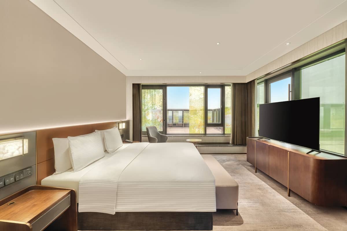 Habitación de hotel moderna con una cama grande, televisión, escritorio y vistas al balcón.
