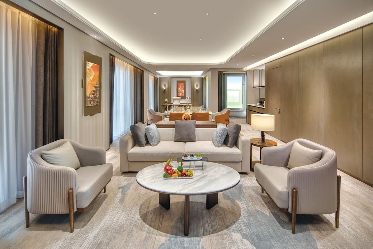 Una habitación de hotel moderna con un conjunto de sofá, una mesa de centro redonda y una zona de comedor al fondo.