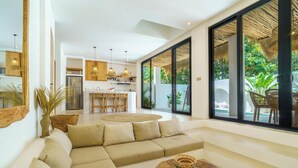 A modern living room with a sectional sofa, a round coffee table, and a dining area with a kitchen in the background. - Stunning 4 BR villa with rooftop - 3 min from Balangan beach (Badung)