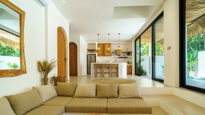 A modern living room with a sofa, a coffee table, and a kitchen in the background. - Stunning 4 BR villa with rooftop - 3 min from Balangan beach (Badung)