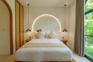 A bedroom with a large bed, two bedside tables, a circular light fixture above the bed, and a view of greenery through a window. - Stunning 4 BR villa with rooftop - 3 min from Balangan beach (Badung)