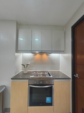 A compact kitchen with a gas stove, oven, and a microwave. - 3BR Apartment with Balcony at One Uptown BGC (Taguig)