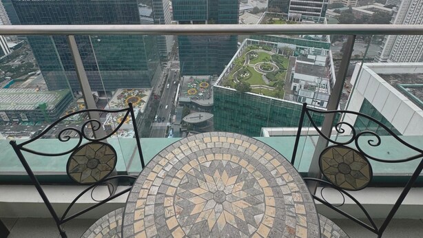 Un edificio de gran altura con vistas panorámicas de la ciudad, una mesa redonda con encimera de mosaico y una barandilla metálica.