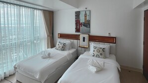 Habitación de hotel con dos camas, un ventanal con cortinas, un cuadro de un paisaje urbano y un cabecero de madera.