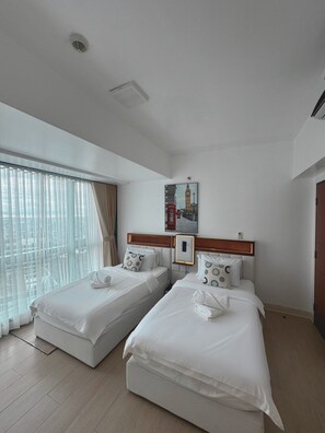 A hotel room with two beds, a large window with curtains, a painting of a cityscape, and a wooden headboard. - 3BR Apartment with Balcony at One Uptown BGC (Taguig)