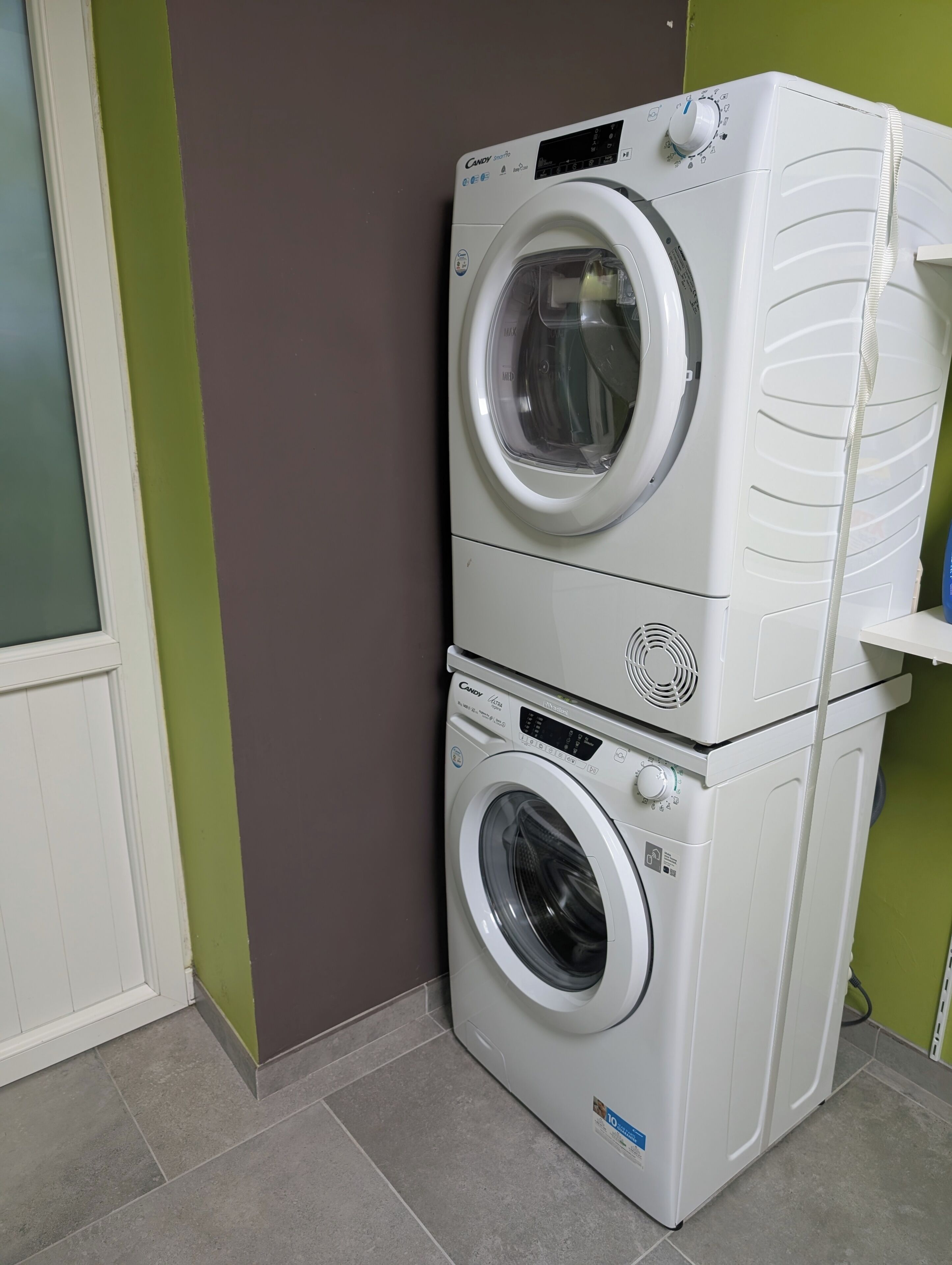 Lavadora y secadora apiladas en una habitación con pared verde y puerta blanca.
