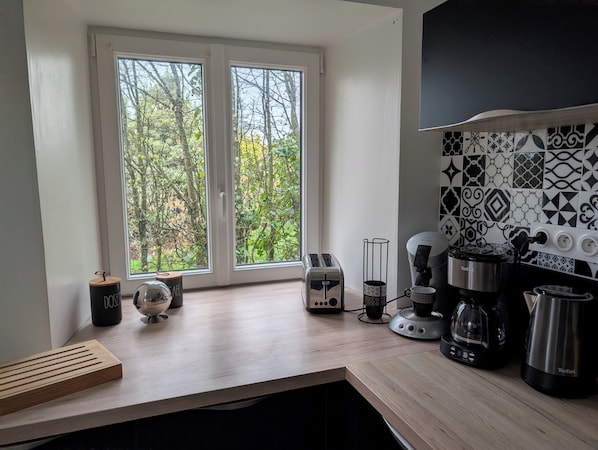 Una cocina con un amplio ventanal, cafetera, tostadora y hervidor.