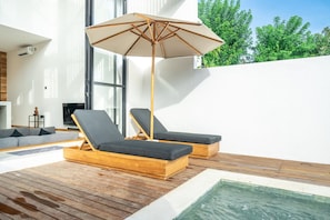 A modern outdoor deck with wooden loungers, a pool, and a large umbrella. - Nunggalan 1 Bedroom Loft Villa with Pool, Walk to Beach (Pecatu)