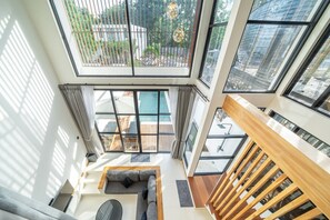 A high-ceilinged room with a view of a pool, a wooden staircase, and a seating area with a sofa and a table. - Nunggalan 1 Bedroom Loft Villa with Pool, Walk to Beach (Pecatu)