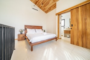 A bedroom with a wooden bed, a nightstand, a potted plant, and a sliding wooden door leading to a bathroom. - Nunggalan 1 Bedroom Loft Villa with Pool, Walk to Beach (Pecatu)