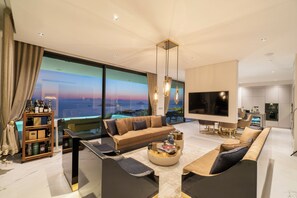 A modern living room with a sofa, coffee table, and TV, large windows with a view, and a wooden shelf with bottles. - Villara Ultra Luxury Daily Housekeeping Private Cook Chauffeur Service (Turgutreis)