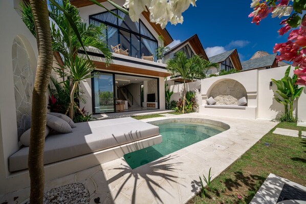Ein modernes Haus mit Swimmingpool, Sitzgelegenheit im Freien und tropischen Pflanzen.