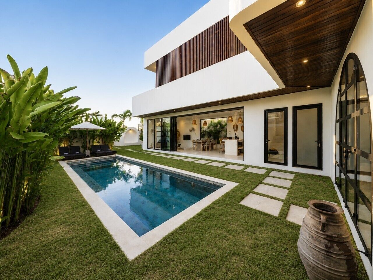 Una casa moderna con piscina, un patio con mobiliario y un amplio ventanal.