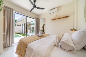 Een slaapkamer met een bed, een plafondventilator, een airconditioning, een nachtkastje, een lamp en uitzicht op een zwembad en terras.