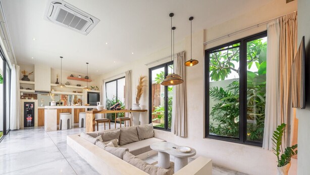 Una sala de estar moderna con un sofá seccional, una zona de comedor y una cocina al fondo.