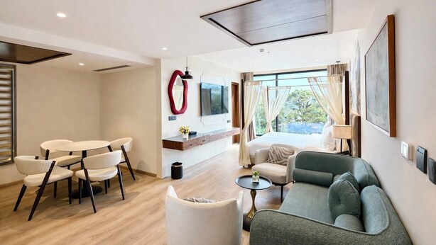 A modern hotel room with a dining area, a sofa, a TV, and a large window with curtains.