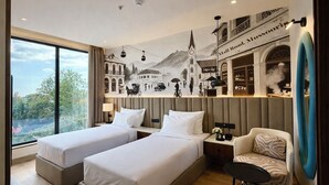 A hotel room with two beds, a sofa, a small table, a view of the outdoors, and a mural depicting a historical scene.