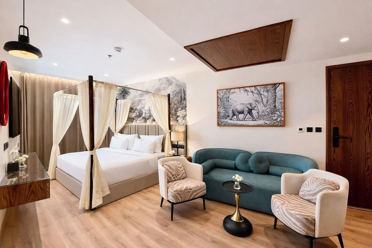 A modern bedroom with a four-poster bed, a sofa, two armchairs, a small round table, and a painting on the wall.