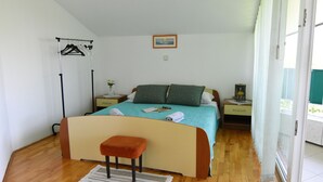 A bedroom with a bed, a bench, a bedside table, a hanging clothes rack, and a window. - Prime Location Apartment Nicely Equipped (Umag)