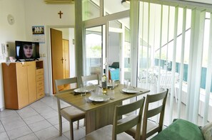 A dining area with a table set for four, a television on a cabinet, and a view through a glass door. - Prime Location Apartment Nicely Equipped (Umag)