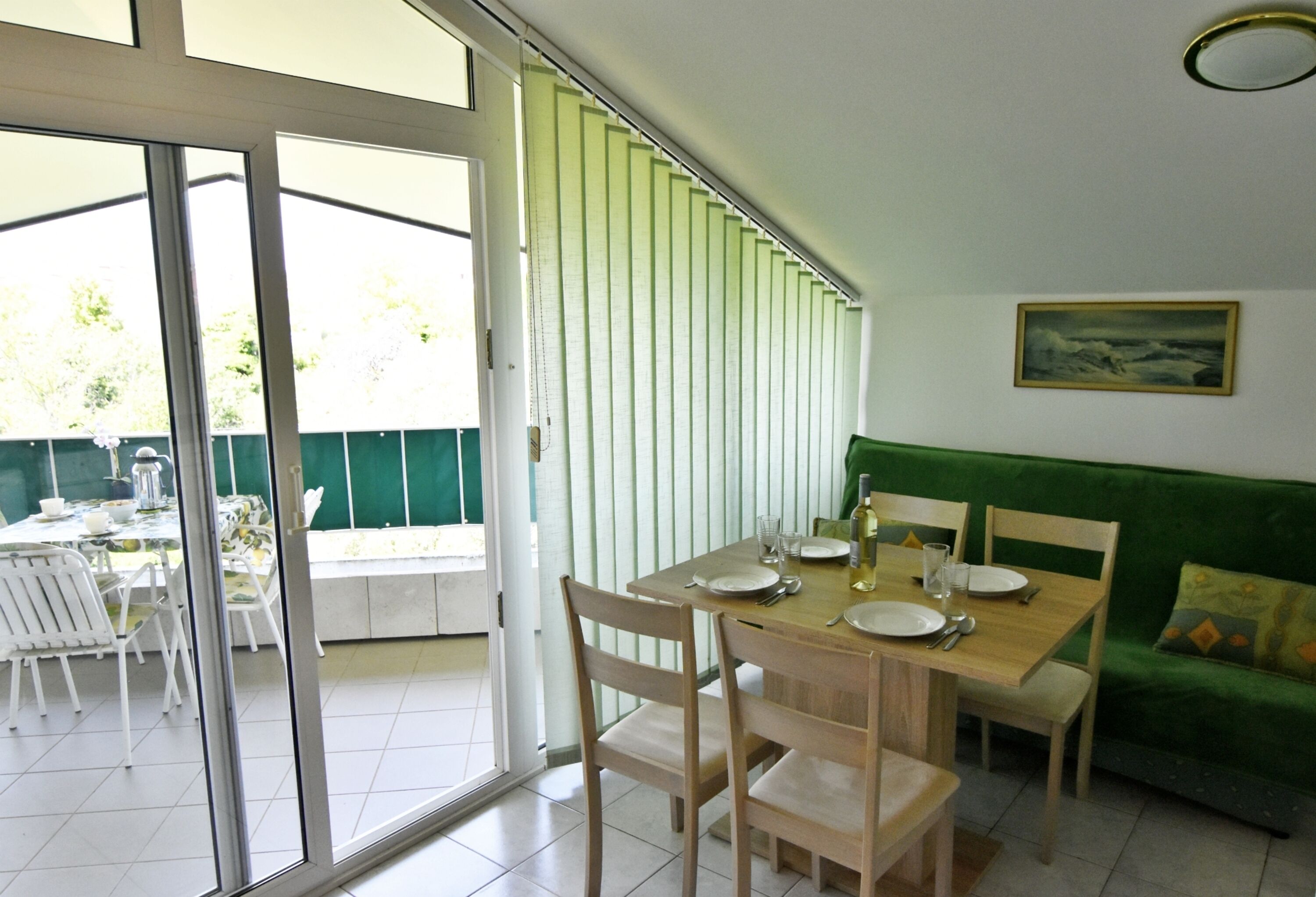 A dining area with a table set for four, chairs, a green sofa, and a sliding glass door leading to an outdoor patio.