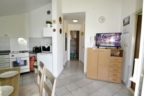 A compact kitchen with a stove, oven, and microwave, a dining area with chairs and a table, and a TV on a wooden cabinet. - Prime Location Apartment Nicely Equipped (Umag)